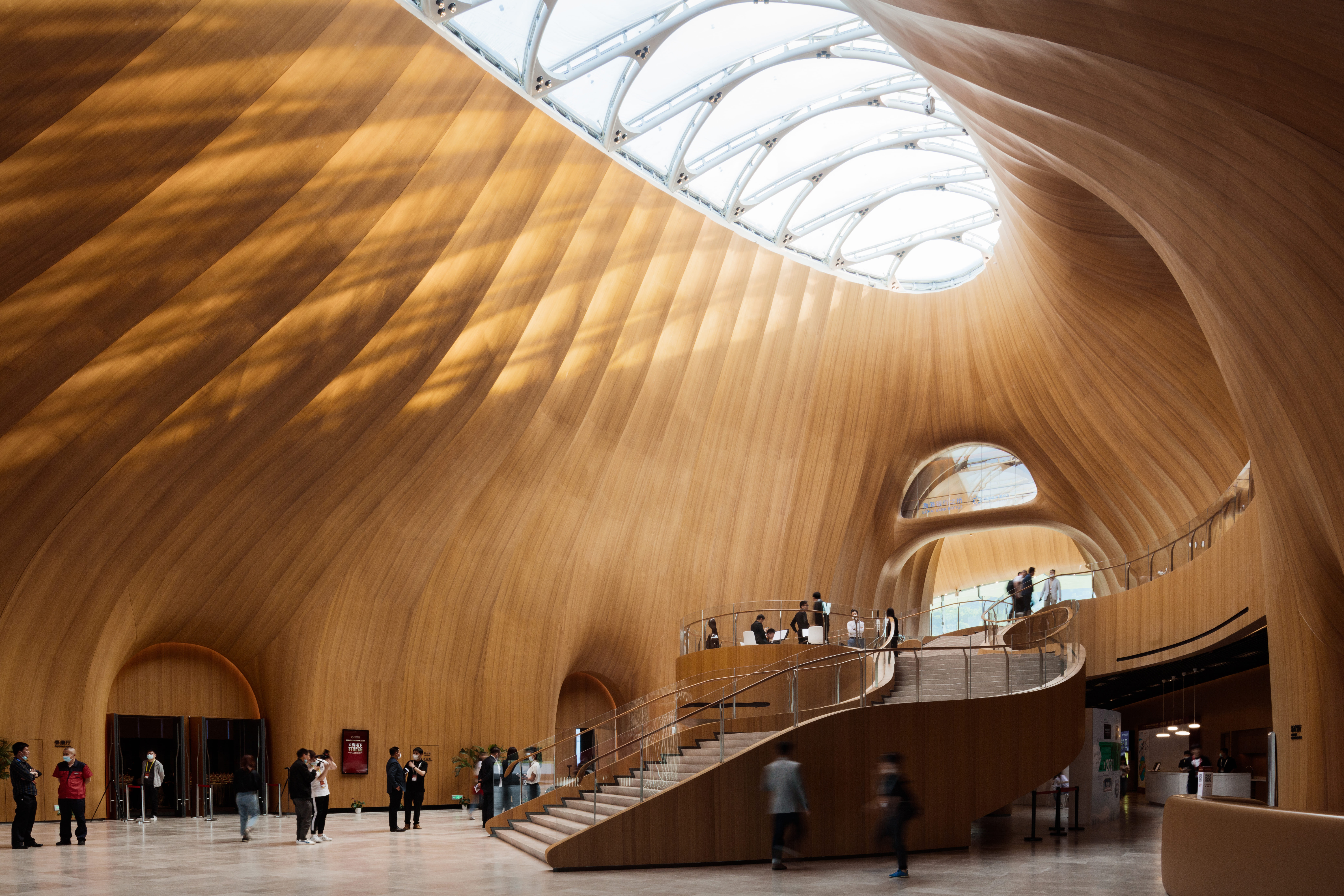 陽光透過天窗灑入木質包裹的大廳，溫暖柔和，層層紋理與屋面白色雪痕設計語言統一。