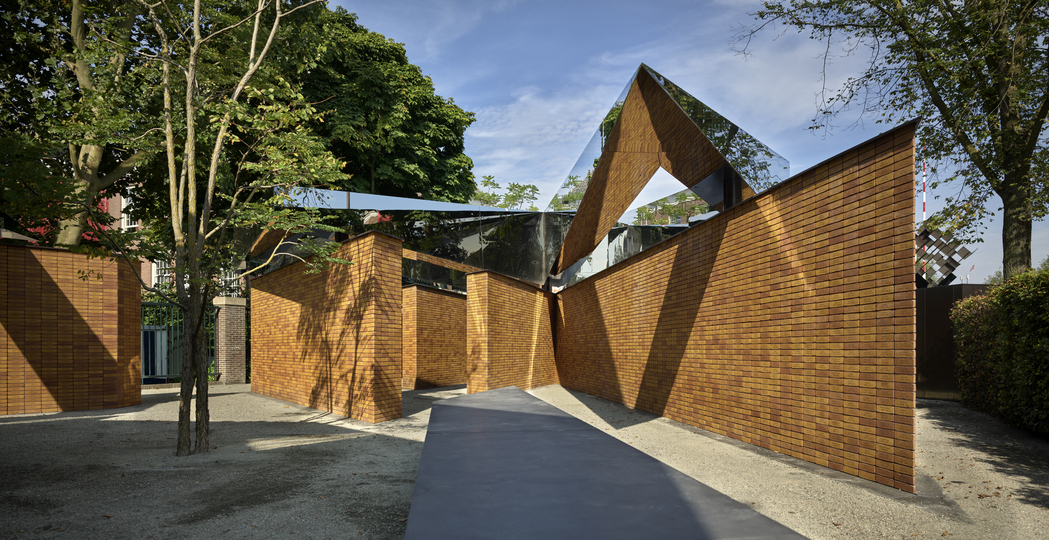 Dutch Holocaust Memorial of Names 在迷宮般的磚牆通道上，架設有代表紀念一詞的不鏽鋼幾何量體。